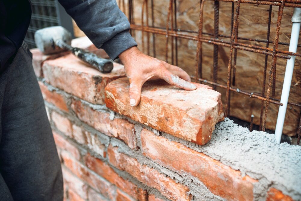 Bricklayer worker installing brick masonry on exterior wall with hands and tools