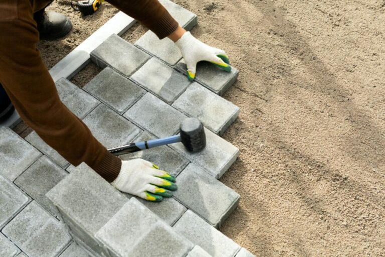 Hands of a worker installing concrete blocks, paving slabs with a rubber hammer