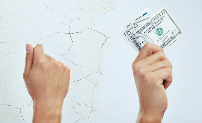 Composite shot of a man holding nothing against a cracked wall while another hand holds bank notes